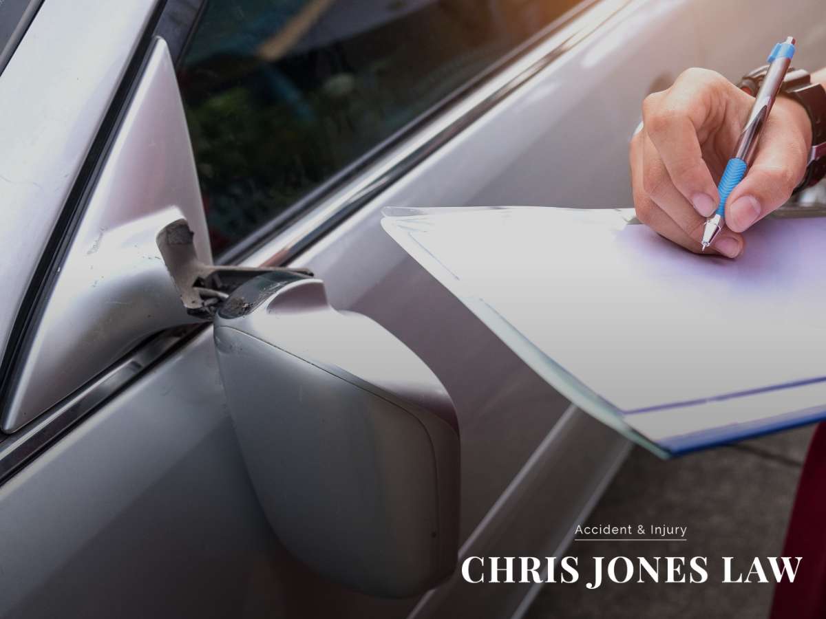 A close-up image of a person writing on a clipboard next to the side mirror of a car, symbolizing the aftermath of a car accident in Arizona, with the logo 'Chris Jones Law' prominently displayed.